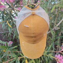 Load image into Gallery viewer, Mustard Distressed Ponytail & Messy Bun Baseball Cap top view with pink flowers and green leaves in the background.