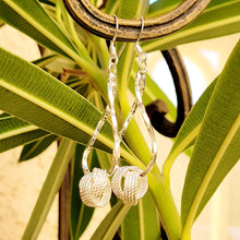Load image into Gallery viewer, Silver twisted knot dangle earrings in a metal post. Green leaves in the background
