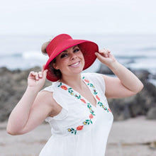 Load image into Gallery viewer, Model is wearing a red bow visor with her hair in a bun. She has on a white dress with flowers. Background of rocks and ocean.