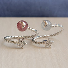 Load image into Gallery viewer, Picture of strawberry stone adjustable ring on the left and moonstone adjustable ring on the right. Rings are sitting on top of a tan surface with blue in the background.