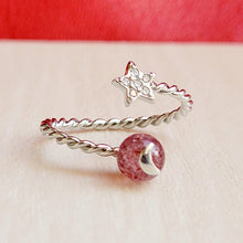 Load image into Gallery viewer, Picture of strawberry crystal ring on a grey surface with a red background.