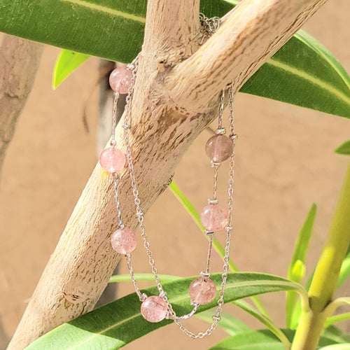 Picture of Double Strand Strawberry Crystal Sterling Silver Bracelet hanging on a tree branch with a tan wall and leaves in the background