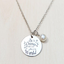 Load image into Gallery viewer, Picture of Be the Change You Wish to See in the World Inspirational Necklace with white charm on a tan background.
