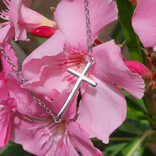 Load image into Gallery viewer, Slanted Cross Sterling Silver Necklace on pink flowers with leaves in the background.