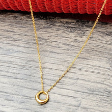 Load image into Gallery viewer, Gold Geometric Charm Necklaces on a grey surface with a red mesh background.
