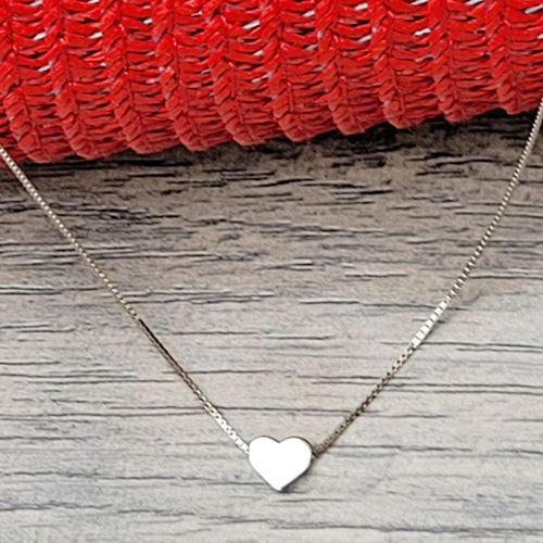 Elegant Heart Sterling Silver Necklace on a grey surface with red mesh in the background. 