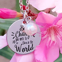 Load image into Gallery viewer, Picture of Be the Change You Wish to See in the World Inspirational Necklace with white charm with pink flowers and green leaves in the background.
