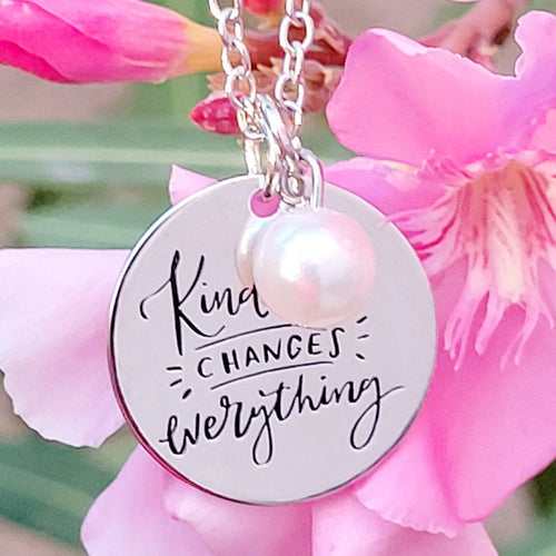 Picture of Kindness Changes Everything Inspirational Necklace against a pink flower with green leaves behind