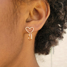 Load image into Gallery viewer, Asymmetrical double heart Sterling silver earring rose gold color on model's left ear with the top heart in a horizontal position. Model has short dark brown curly hair.