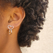 Load image into Gallery viewer, Asymmetrical double heart Sterling silver earring on model's left ear with the top heart in a horizontal position.   Model has short dark brown curly hair.