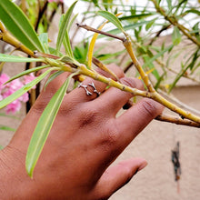 Load image into Gallery viewer, Picture of Leaf Adjustable Sterling Silver Ring on left ring finger against tree and branches with tan wall and trees and pink flower in the background