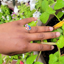 Load image into Gallery viewer, Picture of Flower Two-toned Adjustable Sterling Silver Ring on left ring finger with leaves and white flowers in the background