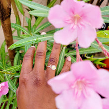 Load image into Gallery viewer, Picture of adjustable daisy ring on right ring finger with pink flowers and green stems in the background