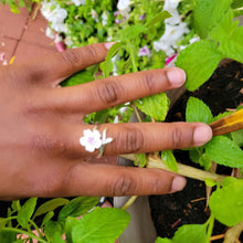 Load image into Gallery viewer, Picture of Plum Flower Adjustable Sterling Silver Ring on a model's left middle finger with leaves and pink flowers in the background.