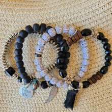 Load image into Gallery viewer, Black Tasseled Beaded Layering Bracelet with all four bracelets laid out separately on a tan mesh background.
