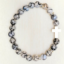 Load image into Gallery viewer, Silver Accent Beaded Cross Bracelet Grey on a tan background.