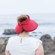 Load image into Gallery viewer, Model is wearing a red bow visor with brown hair in a bun,  She has on a wihte shirt.  There are rocks and ocean in the background.
