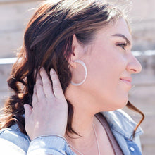 Load image into Gallery viewer, Twisted triple hoop silver earrings on model with long brown hair and jean jacket.  Grey background.
