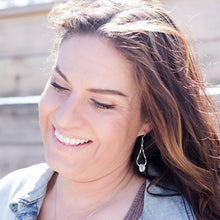 Load image into Gallery viewer, Silver twisted knot dangle earrings on a model with long brown hair. Grey background.
