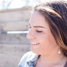 Load image into Gallery viewer, Silver twisted knot dangle earrings on a model with long brown hair.  Grey background.

