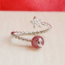 Load image into Gallery viewer, Picture of strawberry crystal ring on a grey surface with a red background.
