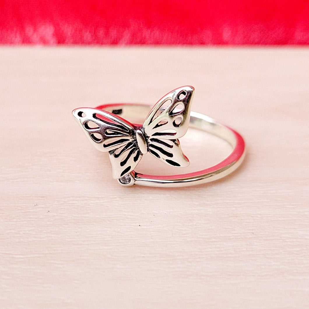 Picture of butterfly zircon adjustable sterling silver ring on tan surface with red in the background.