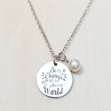 Load image into Gallery viewer, Picture of Be the Change You Wish to See in the World Inspirational Necklace with white charm on a tan background. 
