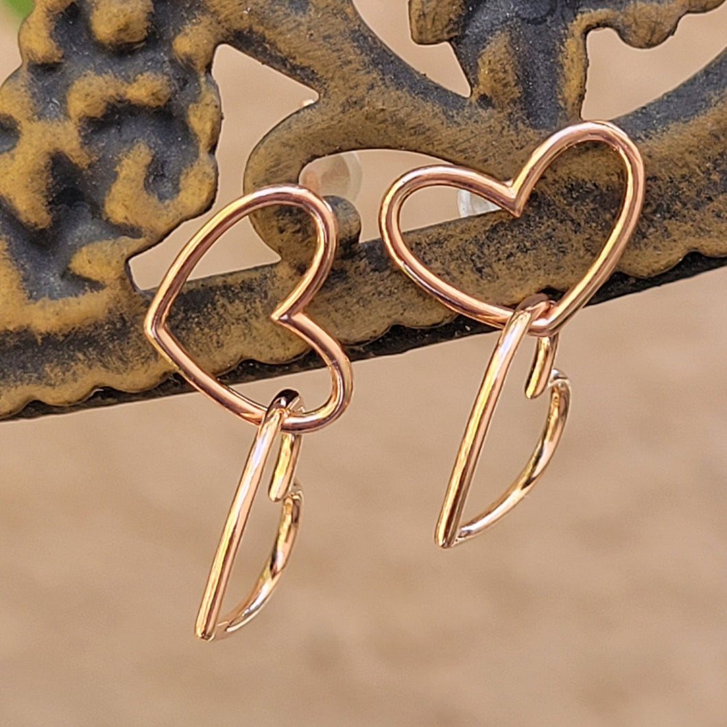 Asymmetrical double heart Sterling silver earring rose gold color on brown post with tan background.