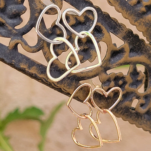 Asymmetrical double heart Sterling silver earring silver color on top and rose gold color on bottom. Both on a brown post with tan background.