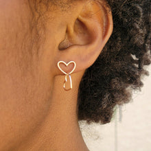 Load image into Gallery viewer, Asymmetrical double heart Sterling silver earring rose gold color on model&#39;s left ear with the top heart in a horizontal position. Model has short dark brown curly hair.
