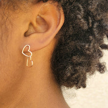 Load image into Gallery viewer, Asymmetrical double heart Sterling silver earring rose gold color on model&#39;s left ear with the top heart in a vertical position. Model has short dark brown curly hair.
