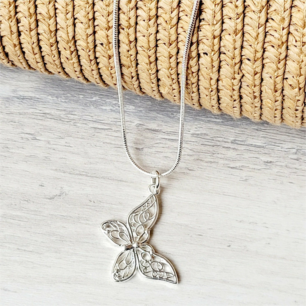 Slanted Butterfly Sterling Silver Necklace on a grey surface with tan mesh background. 