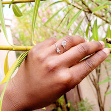 Load image into Gallery viewer, Picture of moonstone ring on left ring finger with model grabbing green plant branches. 
