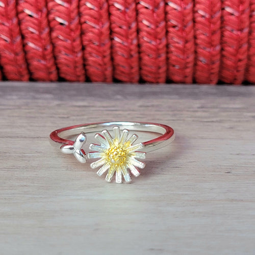 Picture of adjustable daisy ring on a grey tile with a red textured background 