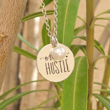 Load image into Gallery viewer, Mom Hustle Disc and Charm Necklace on a branch with leaves in the background. 
