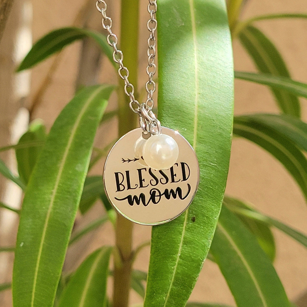 Picture of Blessed Mom Disc and Charm Necklace with white charm and green leaves in the background. 
