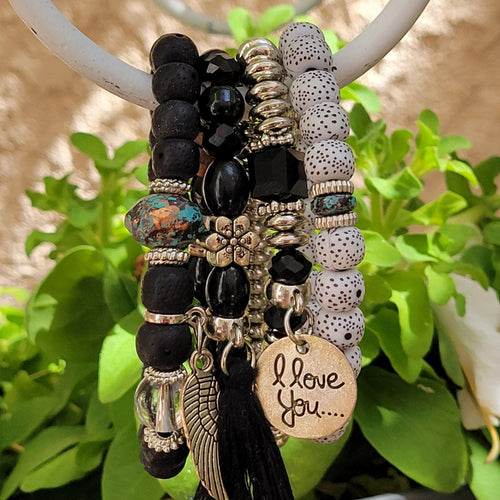 Black Tasseled Beaded Layering Bracelet hanging on white metal hook with green leaves in the background.