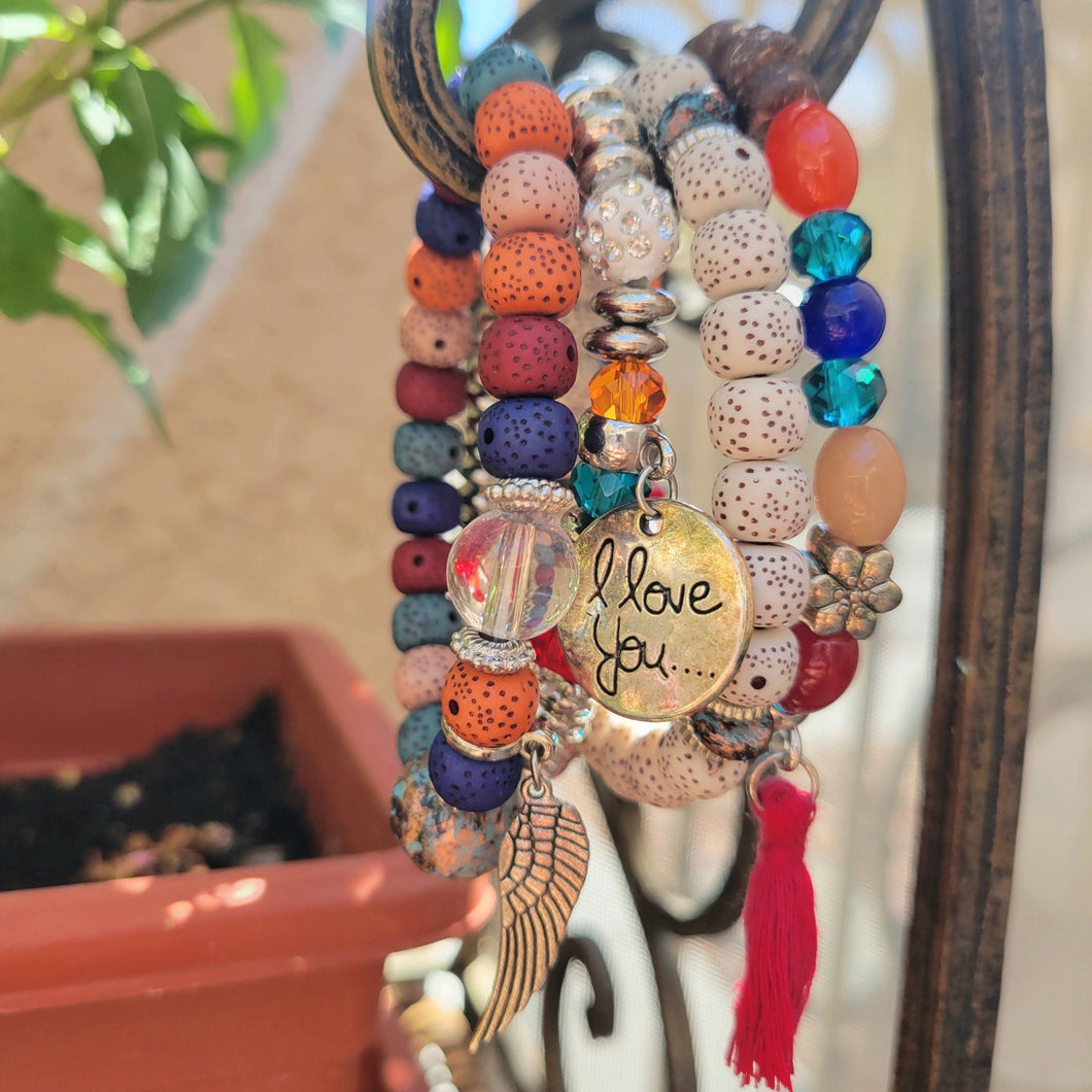 Rainbow Tasseled Beaded Layering Bracelet hanging on white metal hook with green leaves in the background.