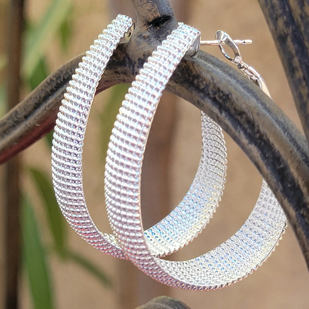 Textured Sterling Silver Hoop Earrings on brown metal with leaves and a tan background. 